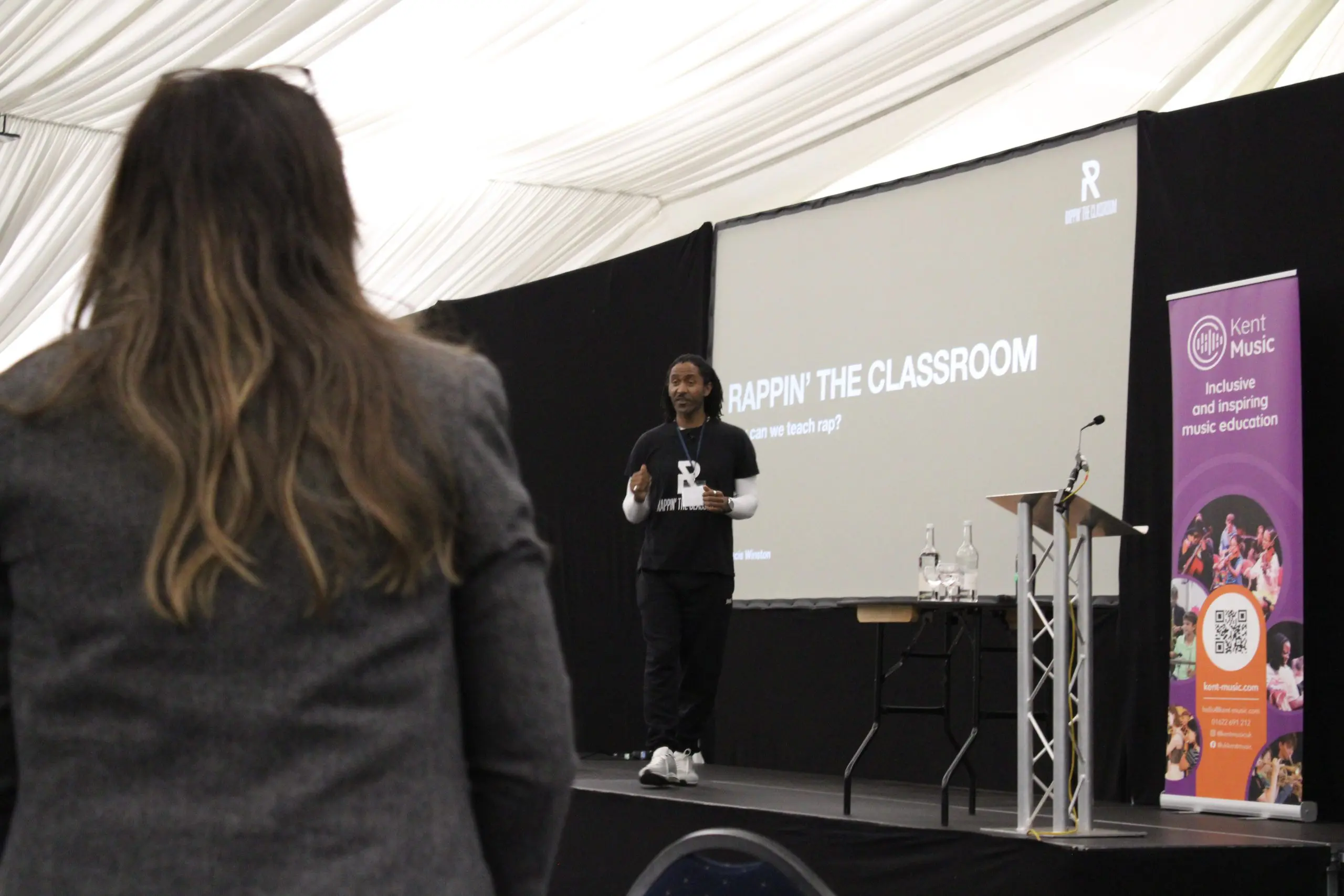 Man on stage delivering a presentation on "Rappin' the Classroom" at the Kent and Medway Music Conference for Kent Music
