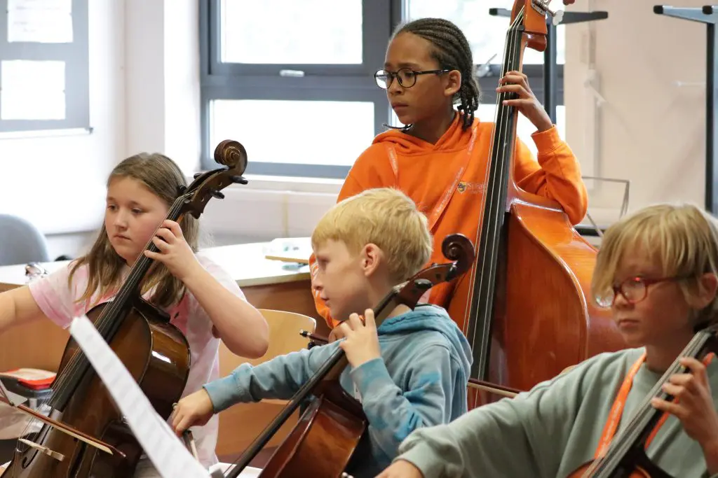 Young students at Kent Music Summer School playing various string instruments including the cello and the double bass.