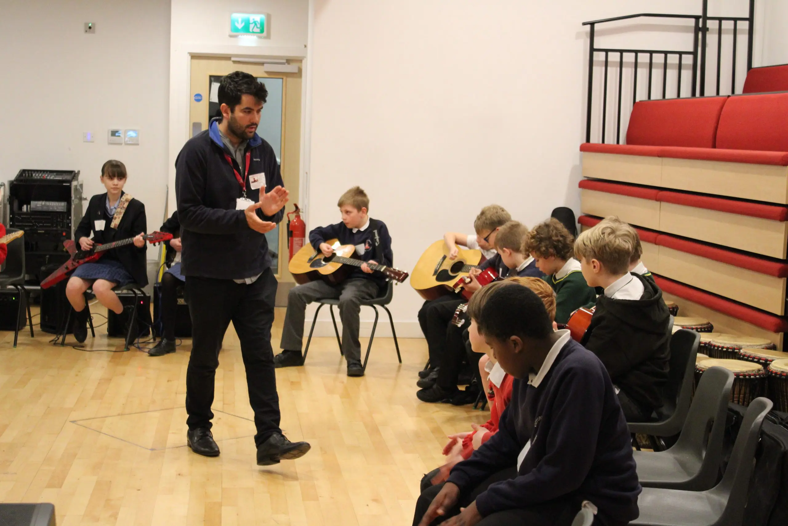 A teacher leading a guitar session with a group of school children